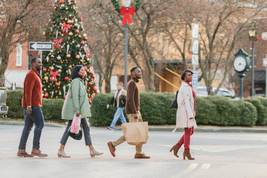 Two Couples walking across River Street with shopping bags and a Christmas tree in the background